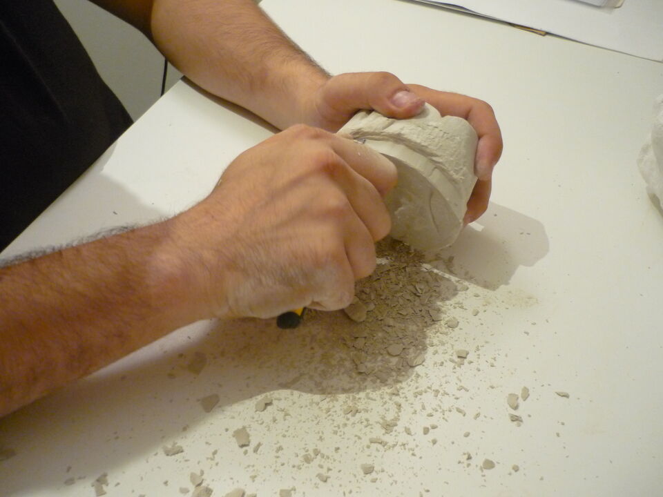 Hands working a piece with a chisel